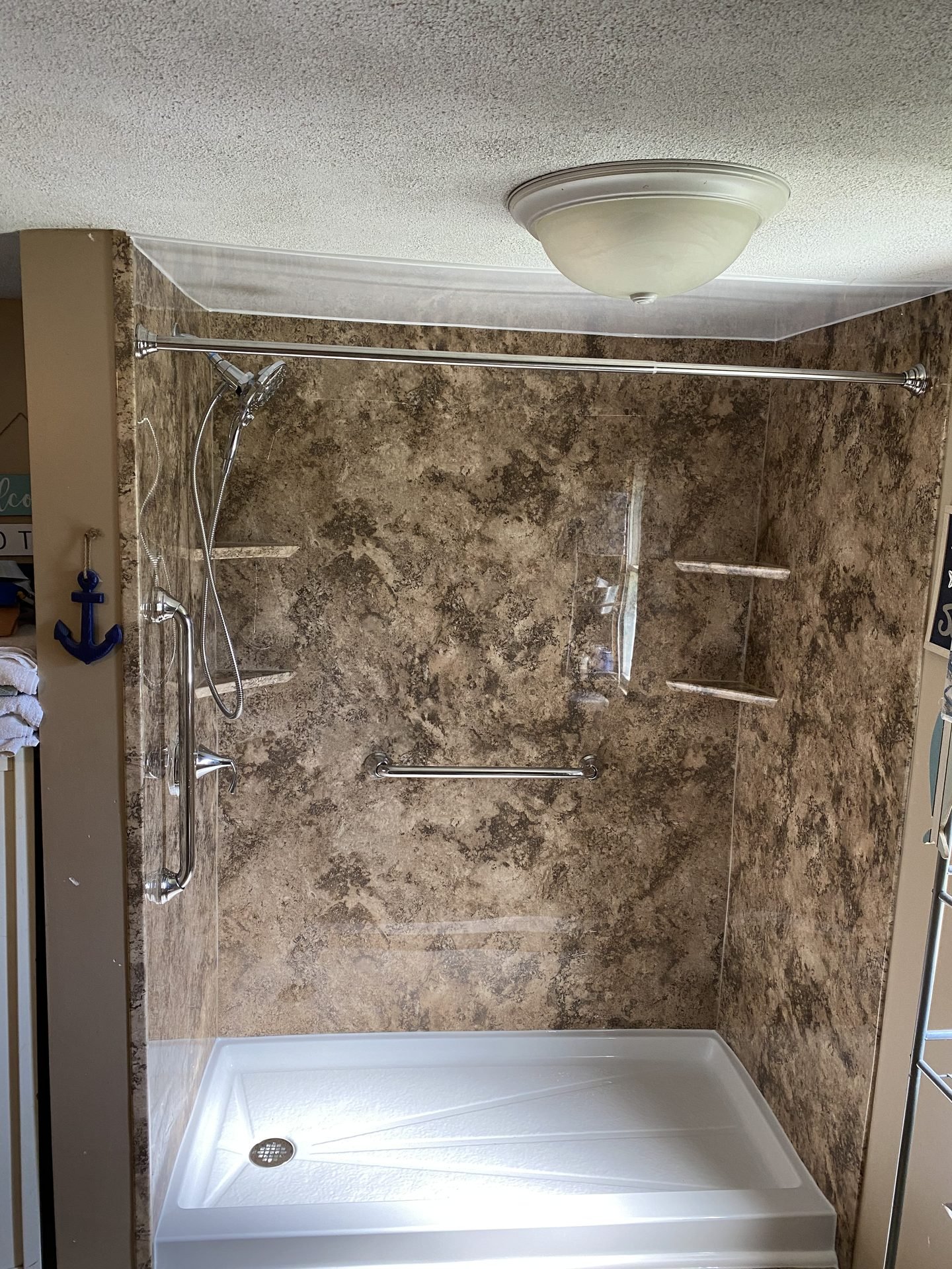 Warm stone-look shower with chrome fixtures and grab bar